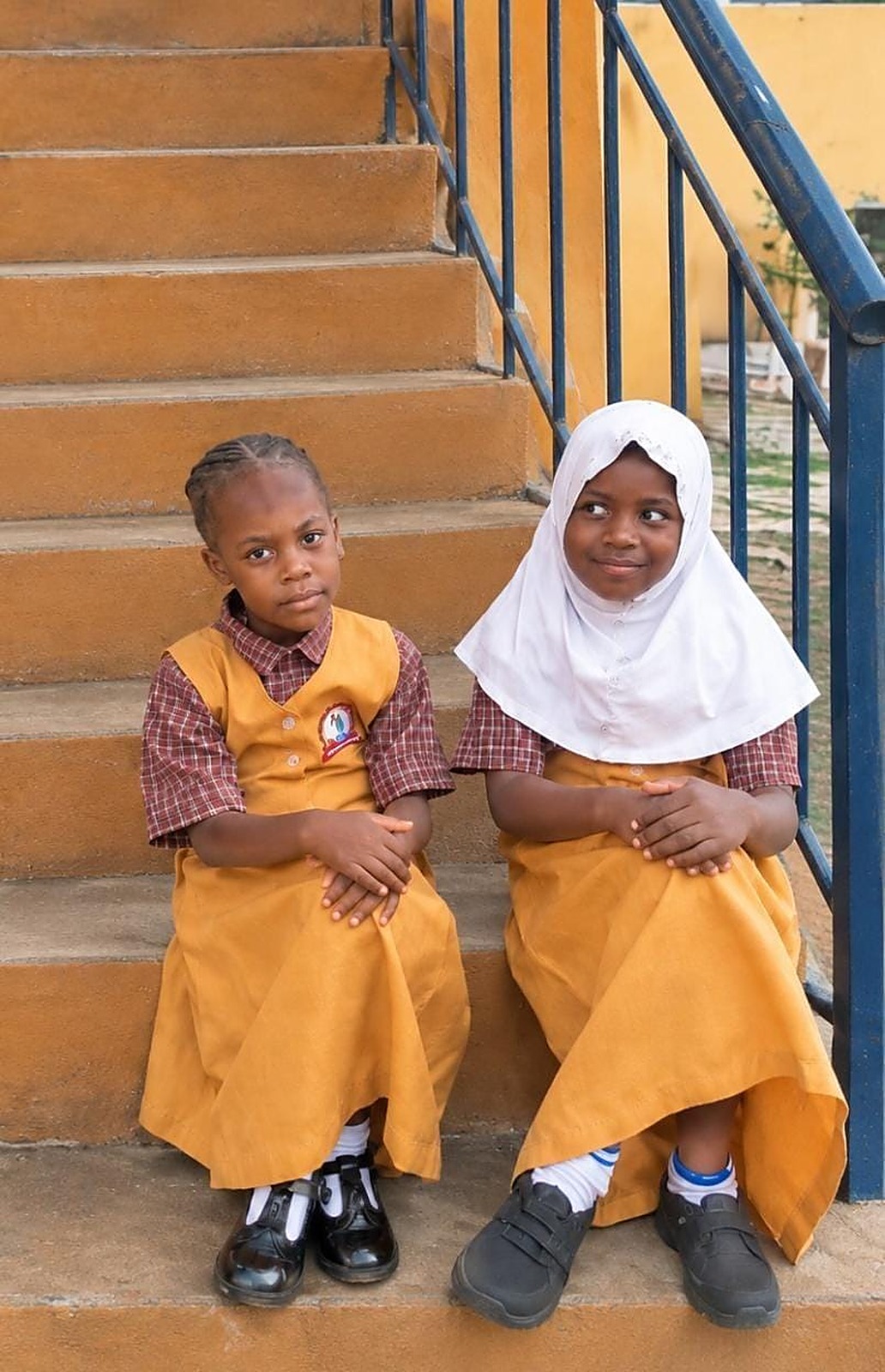 Two young pupils in uniform sitting on the school stairs