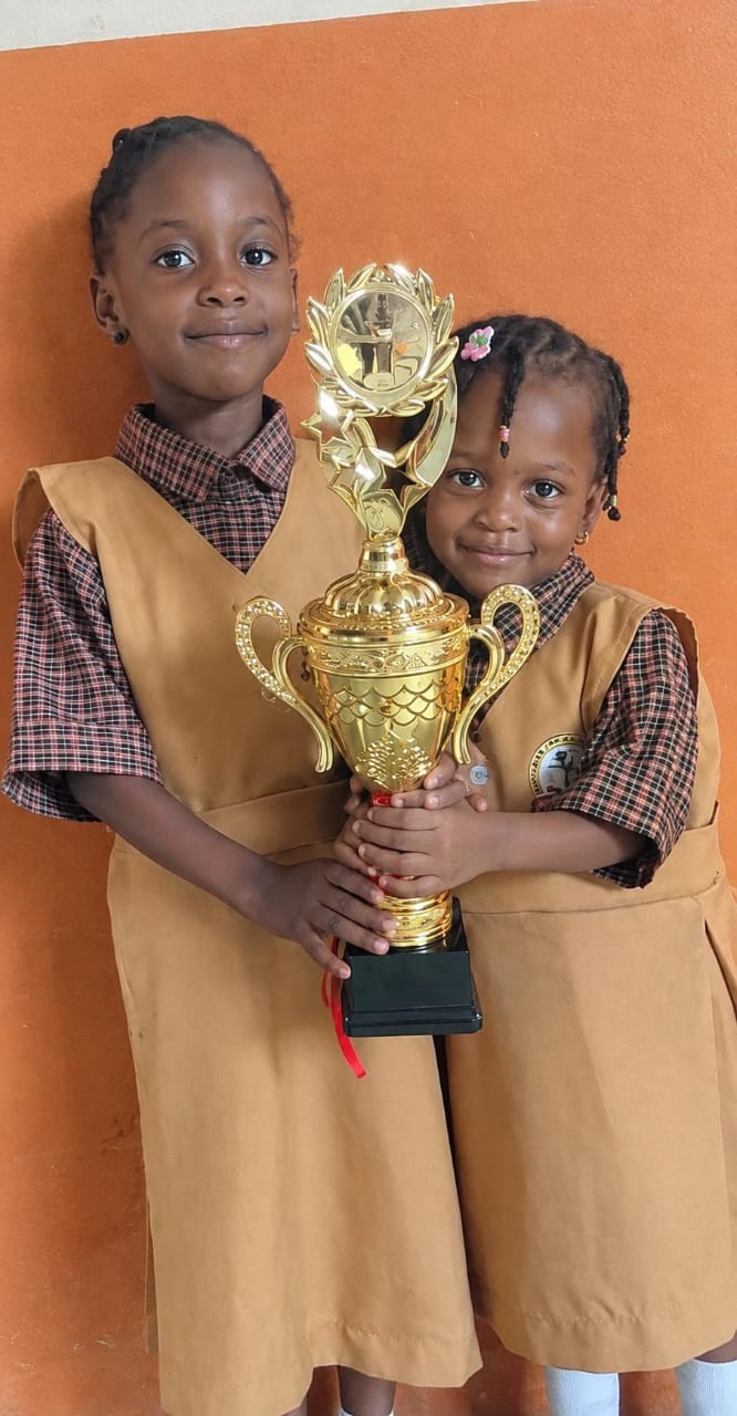Two young Success Private School pupils in uniform holding a trophy together